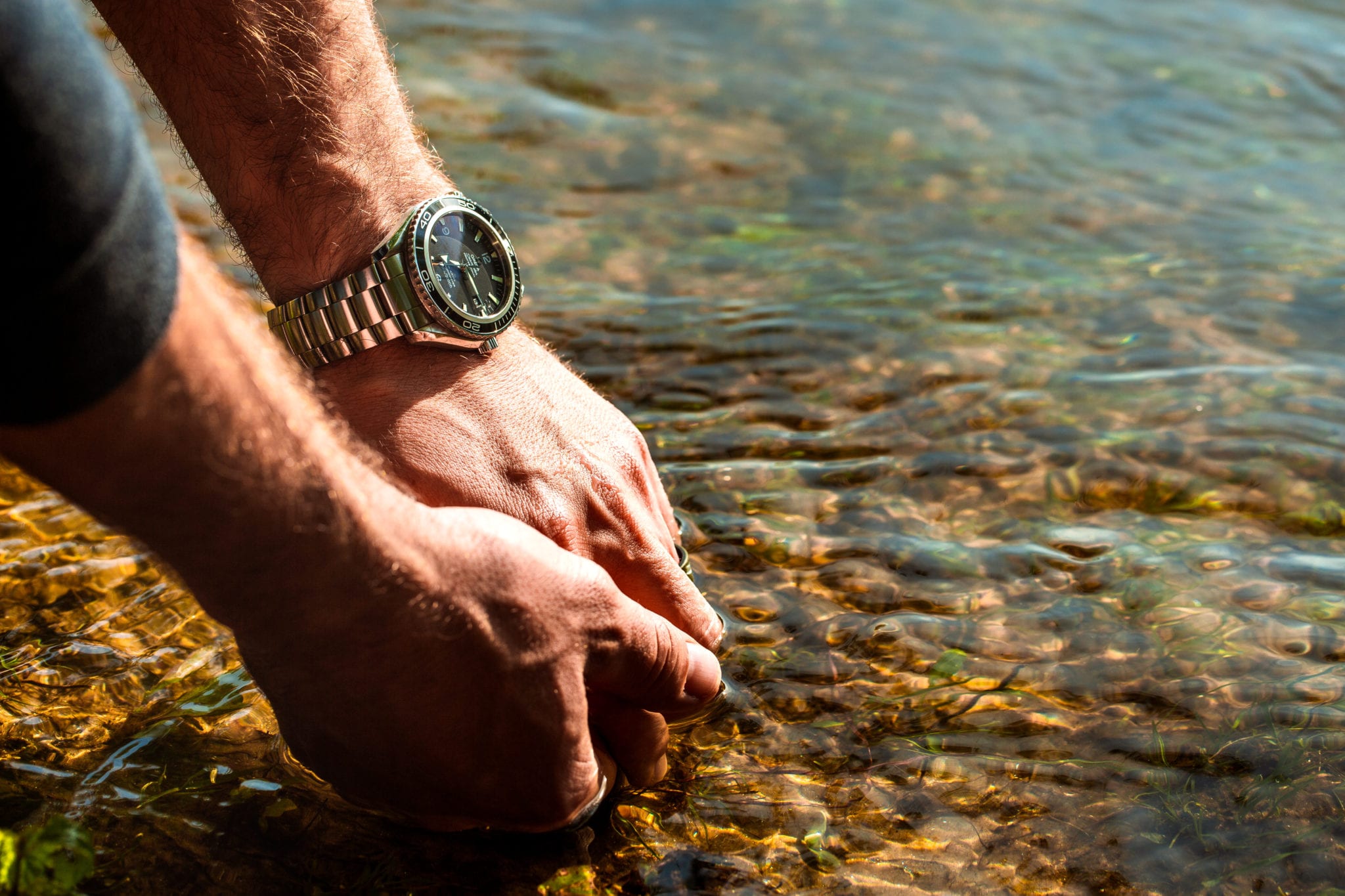 wrist shot of man rinsing hands in the river with a Rolex Explorer on